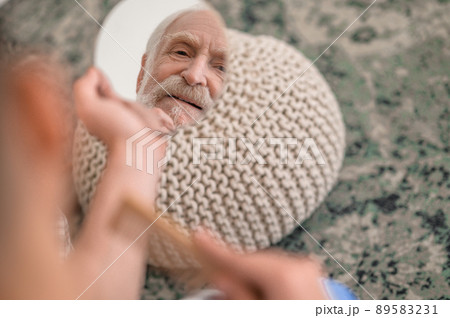 Discontented elderly man examining his reflection in the looking glass 89583231