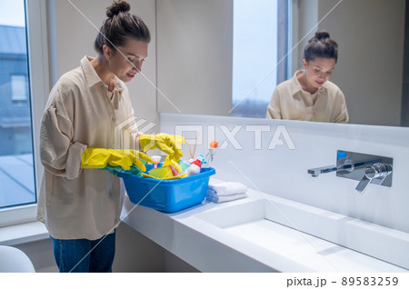A young woman with a box with detergents in the bathroom 89583259