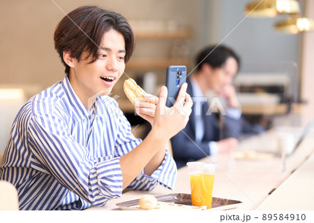 カフェでスマホを見ながら食事をとる若い男性 カフェでスマホを見ながら食事をとる若い男性 89584910