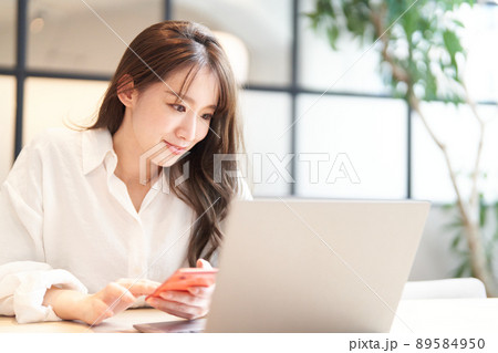 ノートパソコンの画面を見ながらスマホを使う若い女性 ノートパソコンの画面を見ながらスマホを使う若い女性 89584950