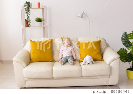 Little girl with cochlear implant sitting on sofa at home. Hear impairment and deaf community concept 89586445