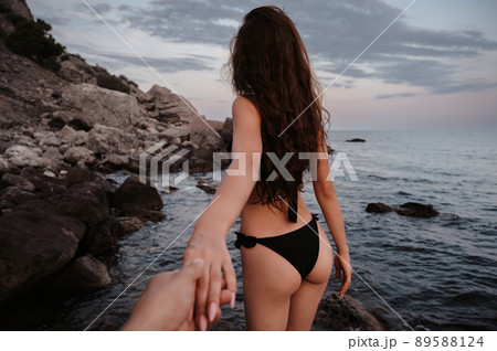Follow me. A beautiful girl with sexy figure in a swimsuit holds her boyfriend's hand on beach by sea 89588124