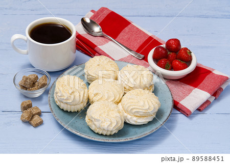 Cup of americano coffee and homemade zephyr or marshmallow in a blue plate on light blue wooden background. 89588451