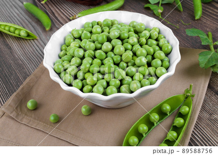 Fresh organic raw green peas in a bowl with peas plants leaves on dark wooden table background, bean protein, close up Fresh organic raw green peas in a bowl with peas plants leaves on dark wooden table background, bean protein, close up 89588756
