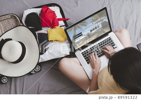 Top view Asian happy woman plan for trip by laptop booking hotel on the bed at home. Women with travel bag use notebook computer internet booking hotel. Holiday summer vacation concept Top view Asian happy woman plan for trip by laptop booking hotel on the bed at home. Women with travel bag use notebook computer internet booking hotel. Holiday summer vacation concept 89591322