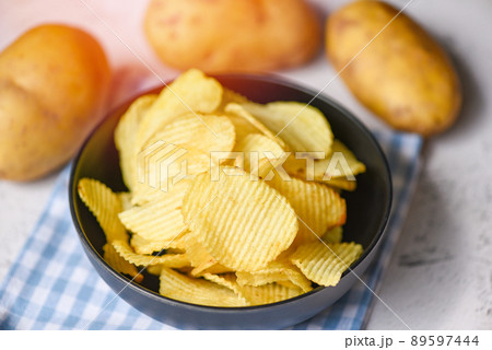 Crispy potato chips on the kitchen table and fresh raw potatoes on wooden background, Potato chips snack on bowl Crispy potato chips on the kitchen table and fresh raw potatoes on wooden background, Potato chips snack on bowl 89597444