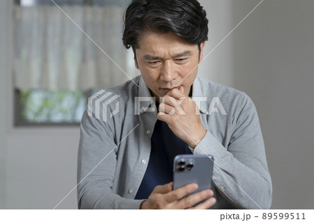 スマートフォンの画面を見ながら考え込むミドルの男性 89599511