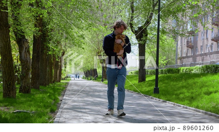 A young man walks with his Pomeranian dog in the park in the morning. The dog is tired and refuses to go. A walk in the fresh air. 89601260