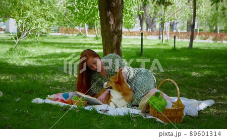 A young woman is relaxing with her dog on a picnic in the park. A girl is reading a book. Picnic in nature A young woman is relaxing with her dog on a picnic in the park. A girl is reading a book. Picnic in nature 89601314
