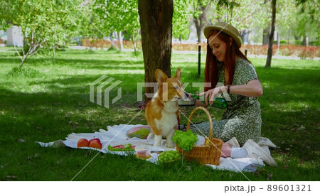 A young woman is relaxing with her dog on a picnic in the park. The girl drinks water from a bottle and pours it into a bowl for the dog. Picnic in nature 89601321