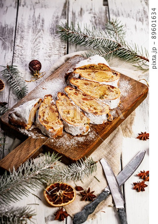 Christmas stollen on a cutting board. Wooden white table background. Traditional Christmas pastry with marzipan, nuts, raisins and dried fruit. Vertical shot 89601634