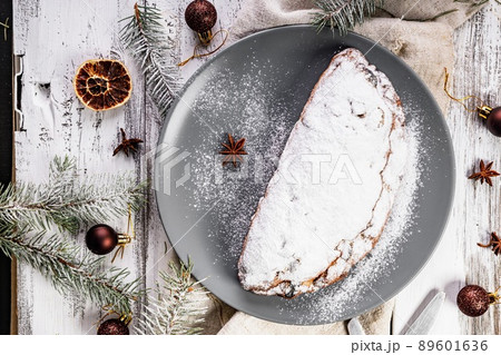Christmas stollen on a gray plate. Wooden white table background. Traditional Christmas pastry with marzipan, nuts and raisins. Top view 89601636