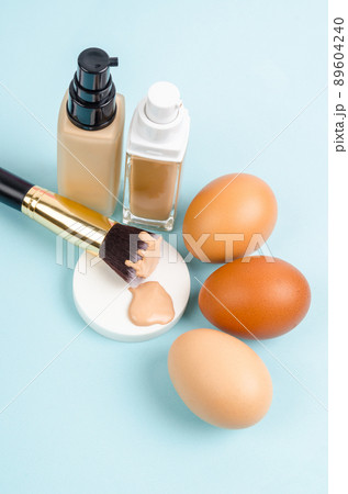 Liquid fluid foundation glass bottle on makeup sponges and egg on blue background. Choose tone color foundation makeup for skin concept. Liquid fluid foundation glass bottle on makeup sponges and egg on blue background. Choose tone color foundation makeup for skin concept. 89604240