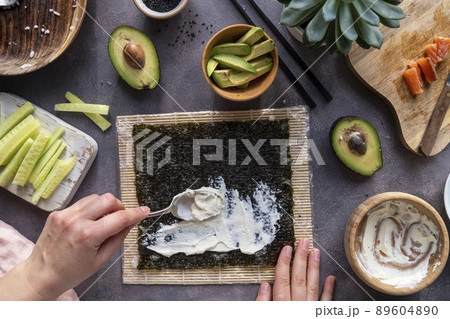 Cooking Sushi rolls at home with salmon, avocado and cucumber. Female hand preparing avocado sushi, step by step. Cooking Sushi rolls at home with salmon, avocado and cucumber. Female hand preparing avocado sushi, step by step. 89604890