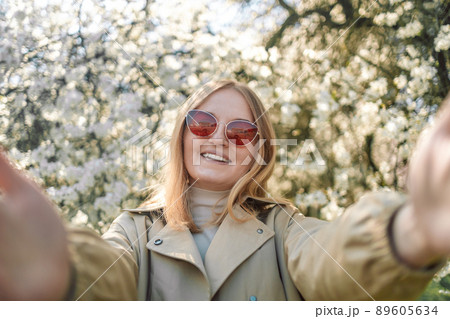 Close-up portrait of happy caucasian cheery young blond girl in red stylish sunglasses taking selfie in park at spring time 89605634