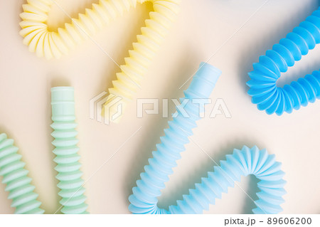 Trendy kids toys pastel colorful pop-tube on beige background. Set of forms and colors corrugated pipe and anti stressing, relaxation fidget finger toys.  89606200
