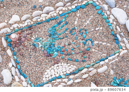 Drawing of a bird is made of multi-colored pebbles on the sea beach. Stones near the coast in summer. Drawing of a bird is made of multi-colored pebbles on the sea beach. Stones near the coast in summer. 89607634