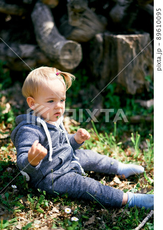 Little girl in overalls sits on the grass near the stumps Little girl in overalls sits on the grass near the stumps 89610095