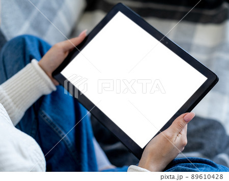 Online education. Digital technology. Mobile mockup. Unrecognizable woman holding tablet computer with blank screen in hands home interior. Online education. Digital technology. Mobile mockup. Unrecognizable woman holding tablet computer with blank screen in hands home interior. 89610428