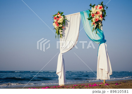 Beautiful summer wedding ceremony outdoors. Wedding arch made of light cloth and white and pink flowers on sea 89610581