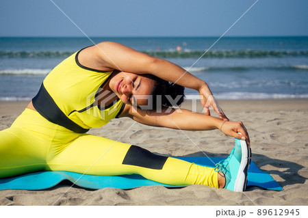 young indian woman practice asanas on blue yogic mat on goa beach . she wearing stylish yellow leggings and fitness top bra 89612945