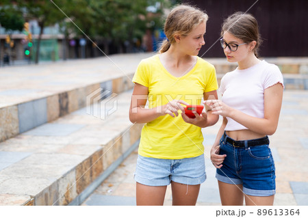 Teenager girls using smartphones while standing in park Teenager girls using smartphones while standing in park 89613364