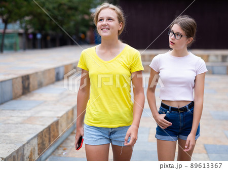 Portrait of two positive girls walking along street of summer city 89613367