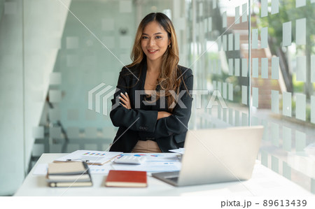 Portrait asian business woman with crossed arms looking at the camera working with laptop computer for accounting financial at office. 89613439