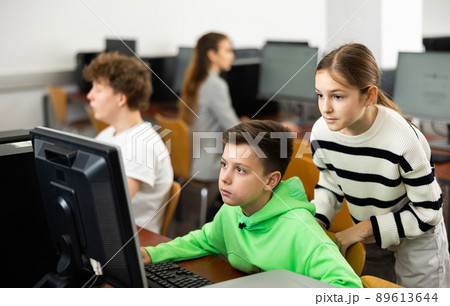 Teenage boy helping young girl with PC problem in computer class 89613644