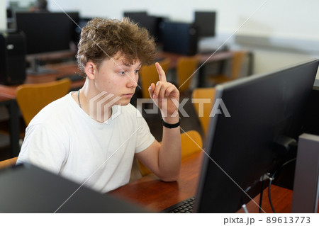 Tired schoolboy with a sore head sits at a computer in classroom Tired schoolboy with a sore head sits at a computer in classroom 89613773