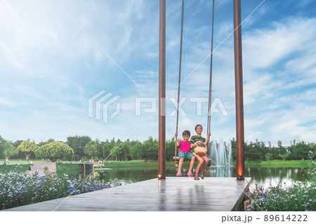 Two asian siblings is swinging on a giant swing in a public park with blue sky. 89614222