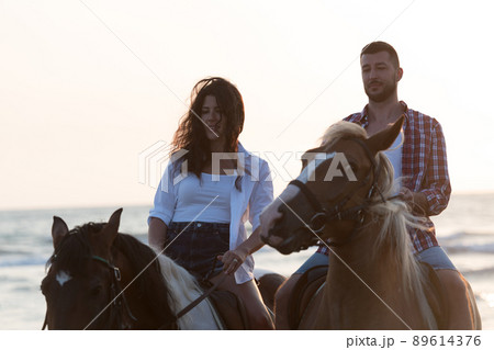 a loving young couple in summer clothes riding a horse on a sandy beach at sunset. Sea and sunset in the background. Selective focus  89614376