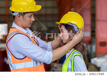 Man puts a safety helmet on woman at factory or plant site. Man puts a safety helmet on woman at factory or plant site. 89617986