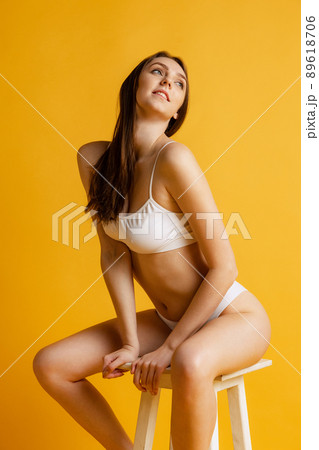 One young beautiful girl sitting on chair, posing isolated over yellow studio background. Taking care after skin One young beautiful girl sitting on chair, posing isolated over yellow studio background. Taking care after skin 89618706