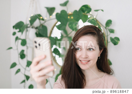 Portrait of a smiling young woman holding smartphone, making selfie or video chatting Portrait of a smiling young woman holding smartphone, making selfie or video chatting 89618847