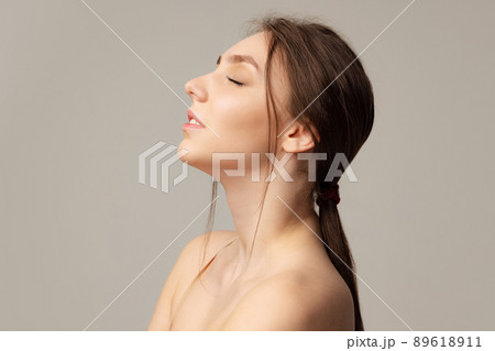 Portrait of young tender woman with low ponytail posing with eyes closed isolated over gray studio background. Natural beauty Portrait of young tender woman with low ponytail posing with eyes closed isolated over gray studio background. Natural beauty 89618911