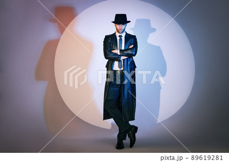 Full length portrait of confident handsome man in black coat and hat with crossed arms posing on studio in the spotlight. Full length portrait of confident handsome man in black coat and hat with crossed arms posing on studio in the spotlight. 89619281