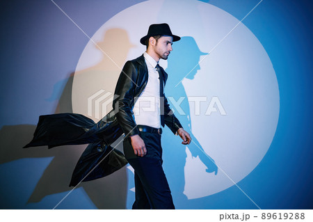 Handsome man in black coat and hat walking like superhero in the spotlight 89619288