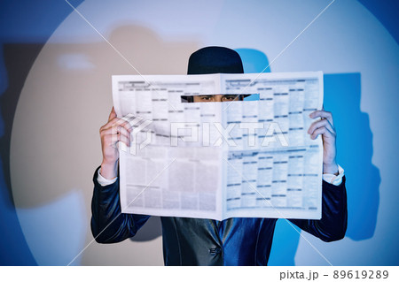 Man hiding watches through the newspaper in the spotlight on studio background 89619289