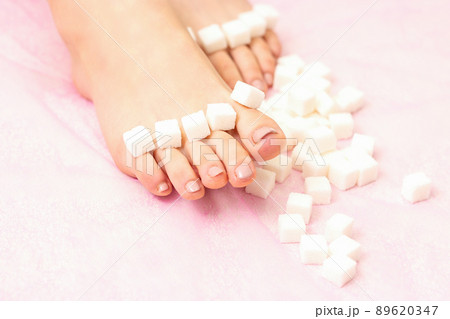 The concept of epilation, waxing. Sugar cubes lying down in a row on female feet, toes over pink background 89620347