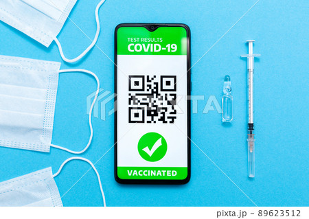 Health and medicine. Electronic Immunity passport with a COVID-19 vaccination stamp and qr-code on a smartphone screen with vaccines, syringe and protective mask on the blue background. Flat lay 89623512