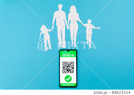 Cellphone with app of digital immunity passport and a silhouette of a family cutted out of paper, with vaccines on a blue background. Flat lay. The concept of vaccination and new normal 89623514