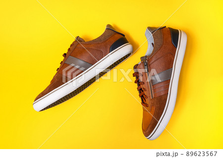 Pair of man's new stylish sneakers made of brown leather on a yellow background. Flat lay. Copy space. Side view of shoes 89623567