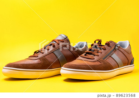 Pair of male's new sneakers made of brown leather beautifully laid out on a yellow background. Close up. Copy space Pair of male's new sneakers made of brown leather beautifully laid out on a yellow background. Close up. Copy space 89623568