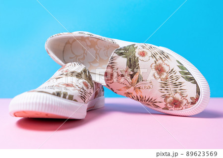 Pair of female's new stylish slip-ons with floral ornament on a pink-blue background. Close up 89623569