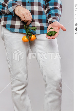 Concept of male sexual diseases. A man at the level of the genitals holds tangerines or oranges on a twig, and holds leaves in his hands. Testicular cancer Concept of male sexual diseases. A man at the level of the genitals holds tangerines or oranges on a twig, and holds leaves in his hands. Testicular cancer 89623570