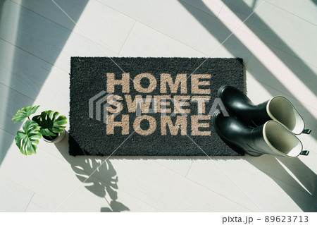 Rain boots on home sweet Home door mat during fall rainy season. Entrance doormat of house homeowner. Top view of rug for floor protection of rain water during autumn. Rain boots on home sweet Home door mat during fall rainy season. Entrance doormat of house homeowner. Top view of rug for floor protection of rain water during autumn. 89623713