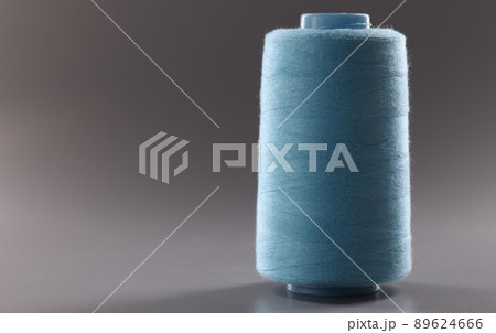 Blue colour thread spool on grey background, thread for dressmaking industry, yarn for sewing Blue colour thread spool on grey background, thread for dressmaking industry, yarn for sewing 89624666