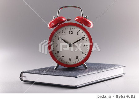 Red retro clock stand on top of closed book or diary, time to study, time to learn new information Red retro clock stand on top of closed book or diary, time to study, time to learn new information 89624683