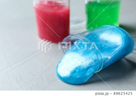 Overturned plastic container with light blue slime on grey background. Space for text 89625425